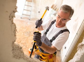 En man van middelbare leeftijd is bezig een muurtje weg te breken met hamer en bijtel.